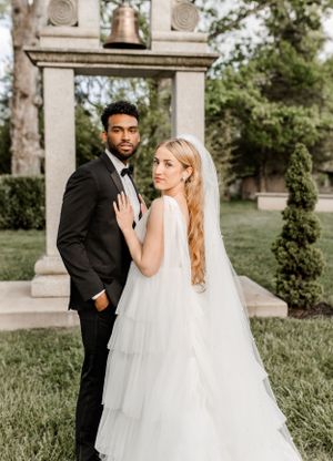 A romantic outdoor wedding portrait in front of a stone bell tower with a flowing white bridal gown.