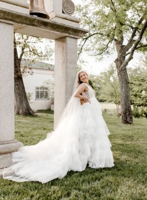 Bride in flowing white gown with long train twirls joyfully in garden setting.