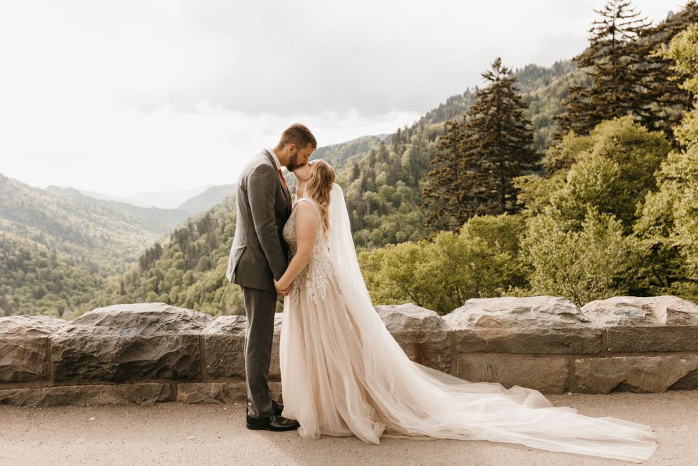 Bride and groom share a tender embrace on a stone overlook with sweeping mountain scenery.