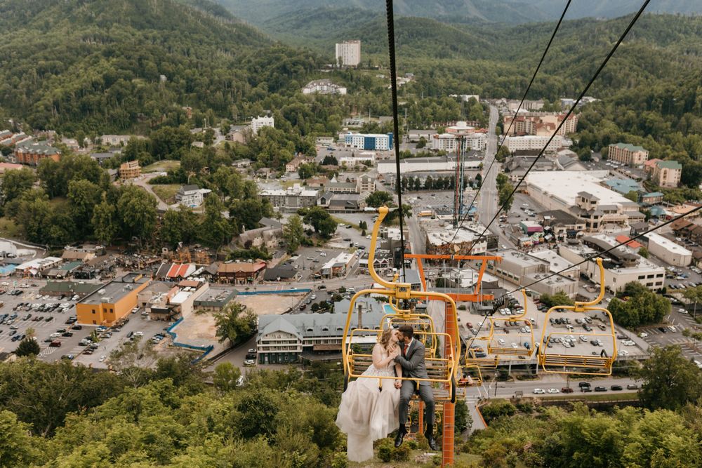 Aerial view of wedding couple on chairlift descending over Gatlinburg city below.