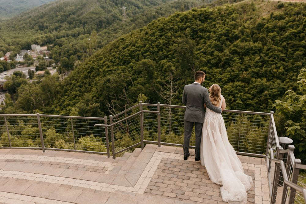 Wedding couple walks hand-in-hand on stone steps with stunning mountain valley views in the background.