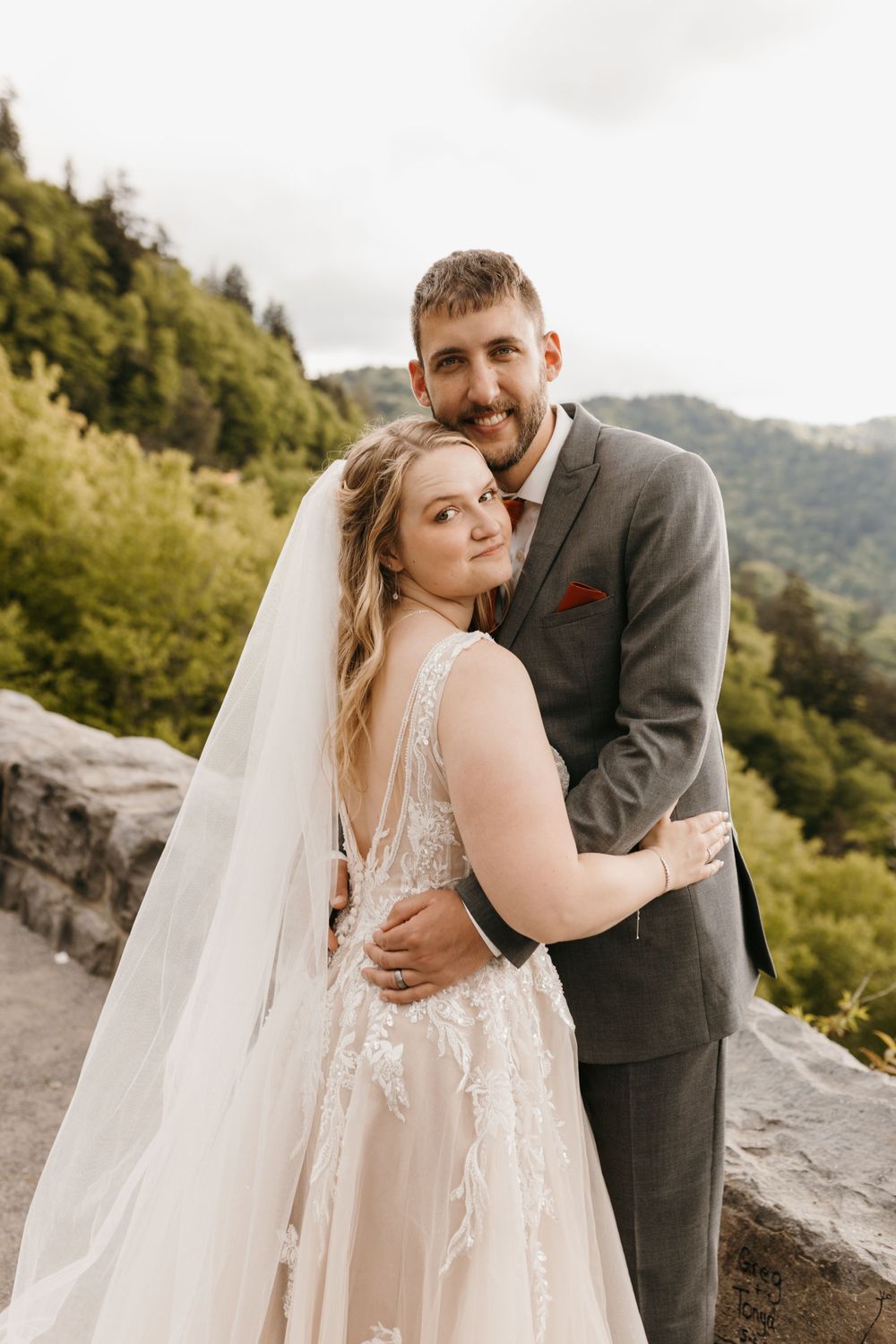 Bride and groom embracing with lush mountain backdrop on their wedding day.