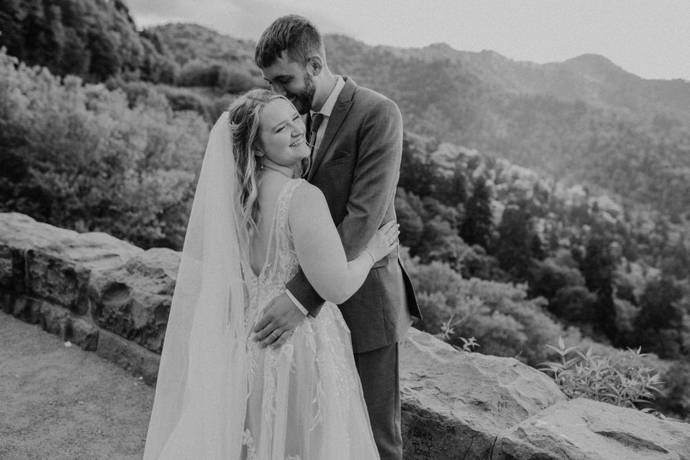 Black and white photo of bride and groom embracing with mountain landscape behind them.