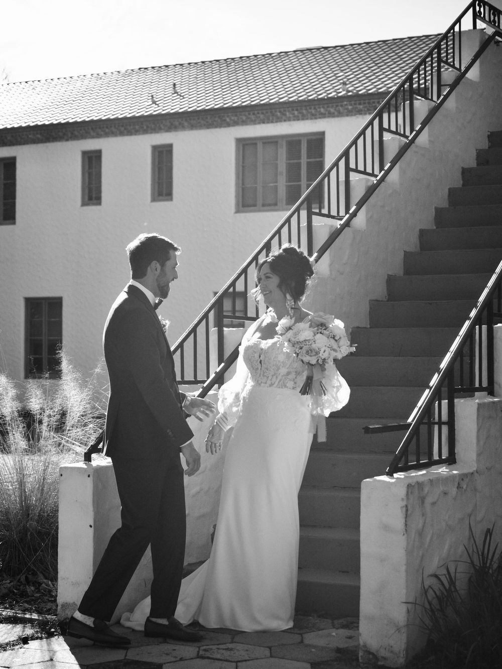 Black and white sequence of newlyweds ascending outdoor stairs at a venue.