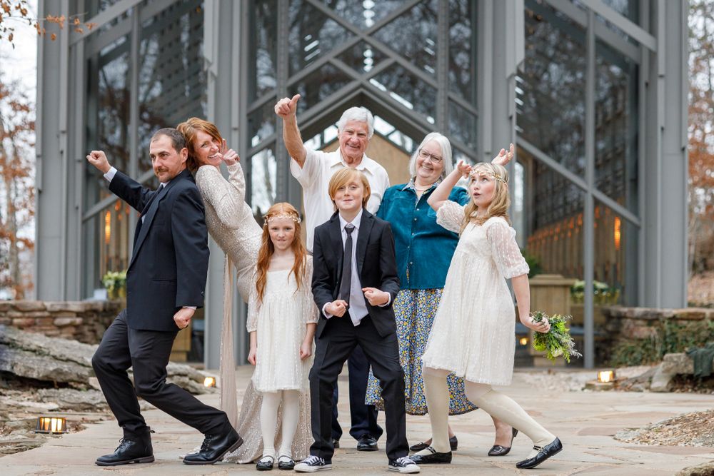 Wedding party jumps and celebrates outside modern glass chapel.