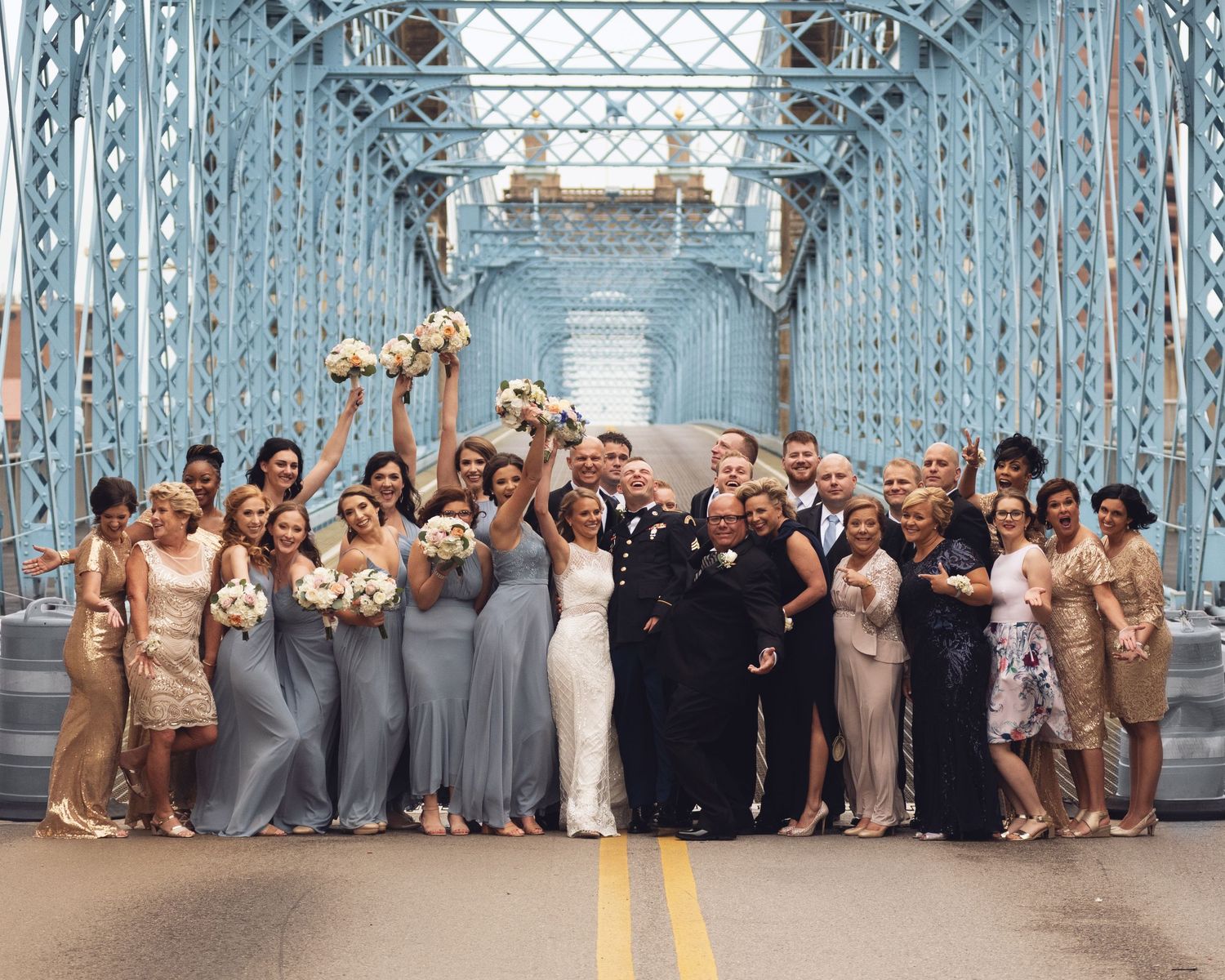 Large wedding party poses together on a blue steel bridge for group photos.