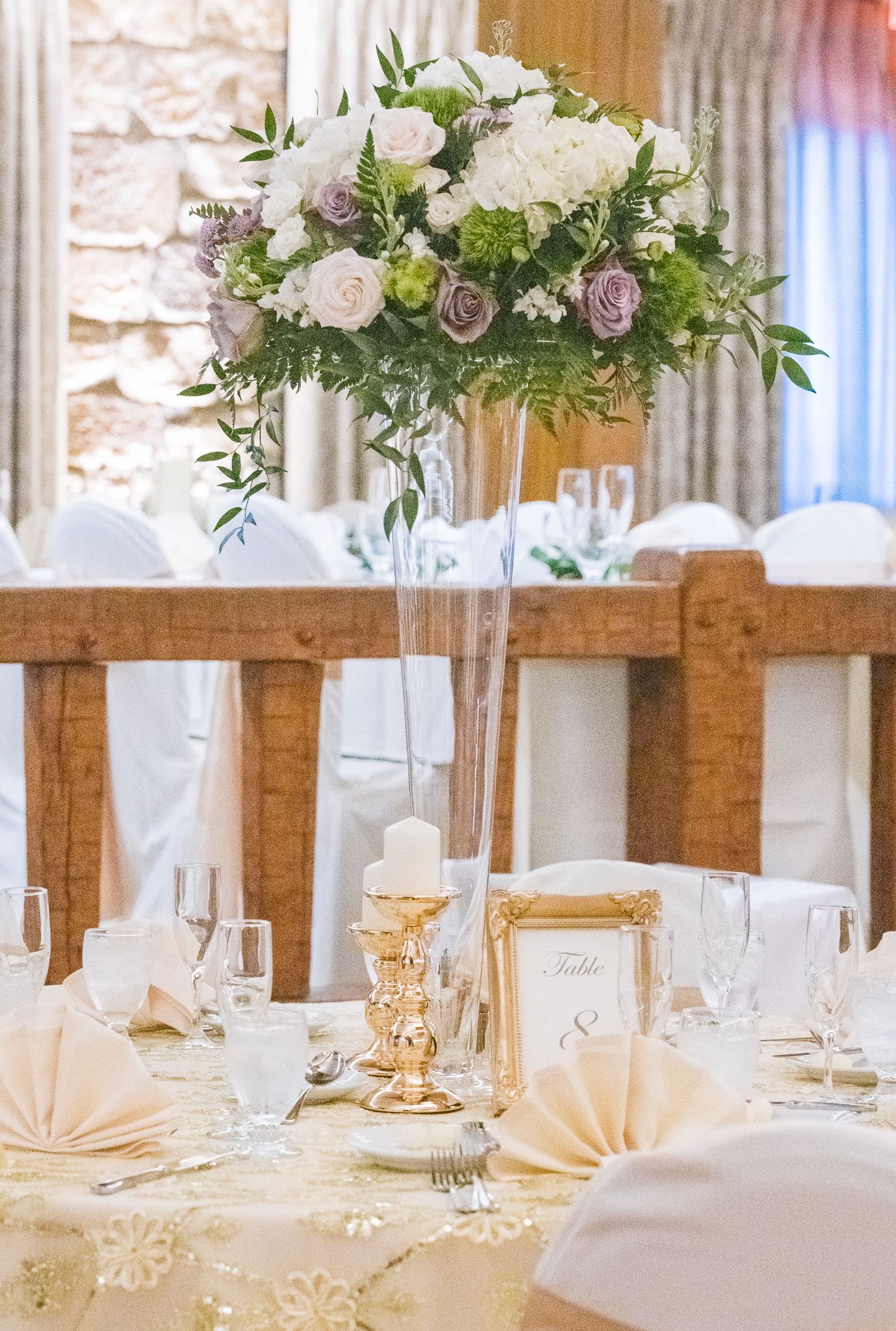 Romantic wedding centerpiece with white and purple roses in tall glass vase on elegant table setting.