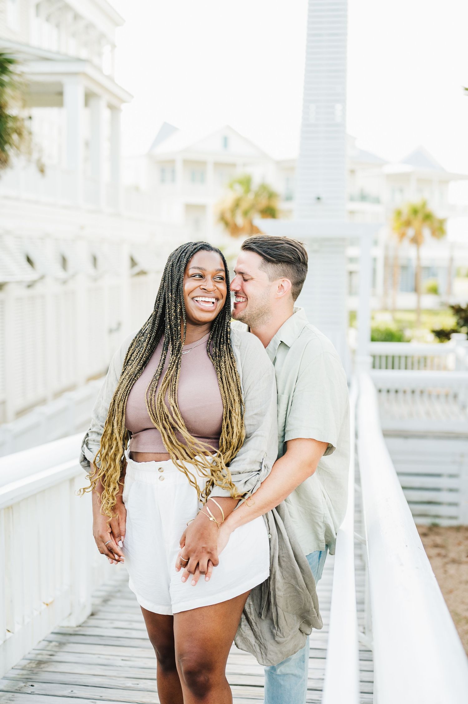Romantic couple sharing intimate moments on a white boardwalk by the beach.