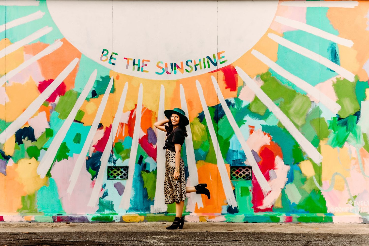A portrait of Jette McCormick standing in front a mural called Be the Sunshine.