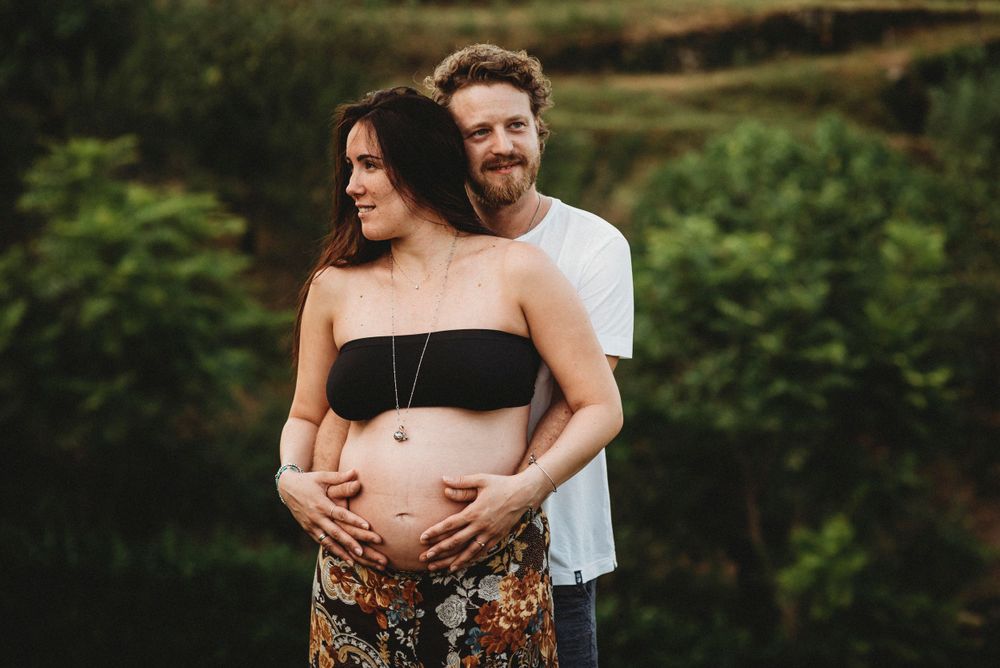 An outdoor maternity photo showing an expectant couple in a natural setting at sunset.