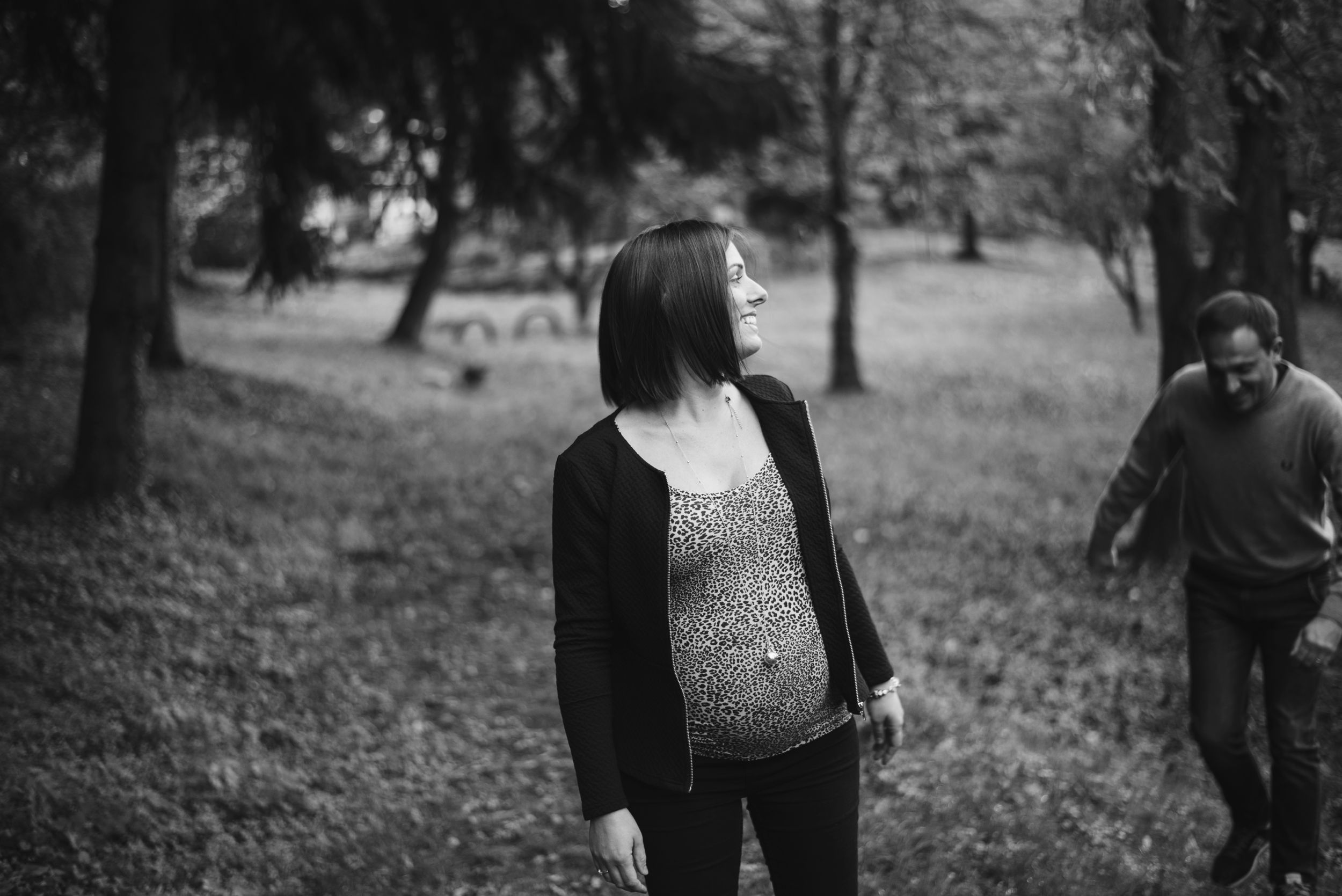 Black and white maternity photo of couple walking through a wooded park.