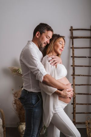 A tender indoor maternity portrait with rustic ladder and floral decor.