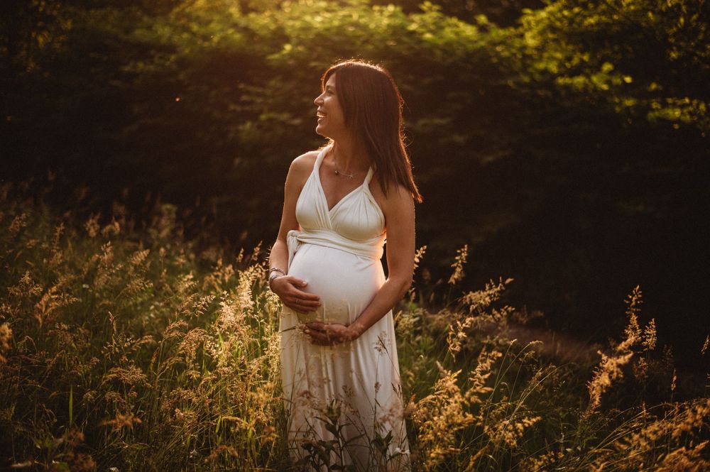 Maternity portrait in white lace dress during golden hour in wildflower field.