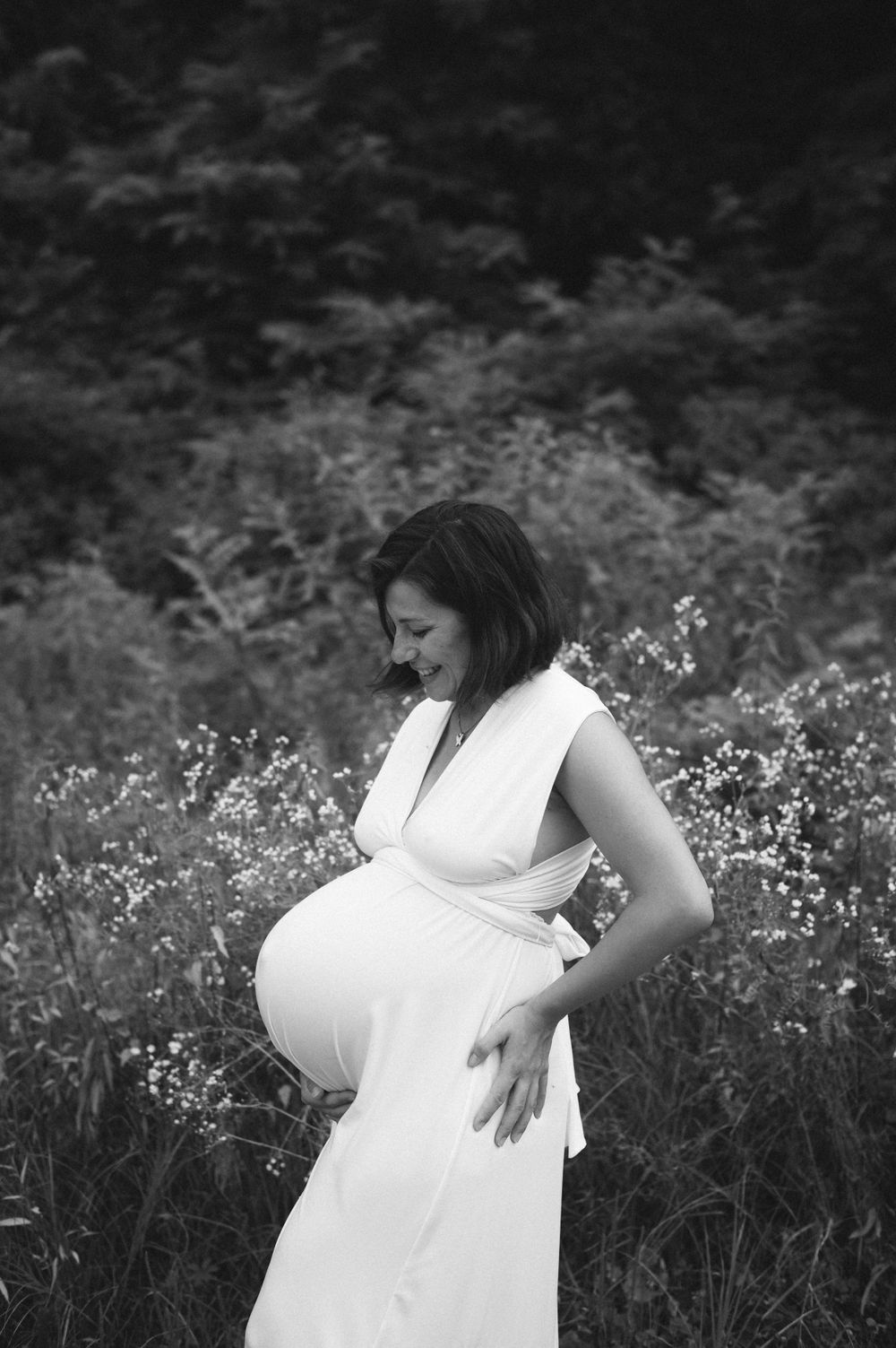 Black and white maternity portrait among wildflowers in sleeveless white dress.