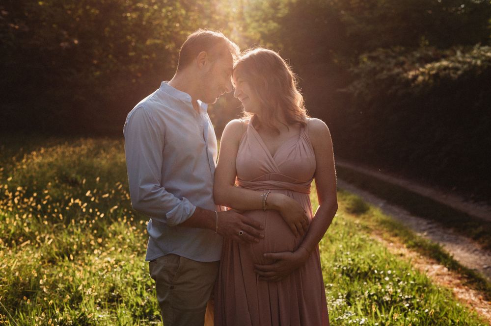 Couple embraces during sunset maternity photoshoot in a meadow.