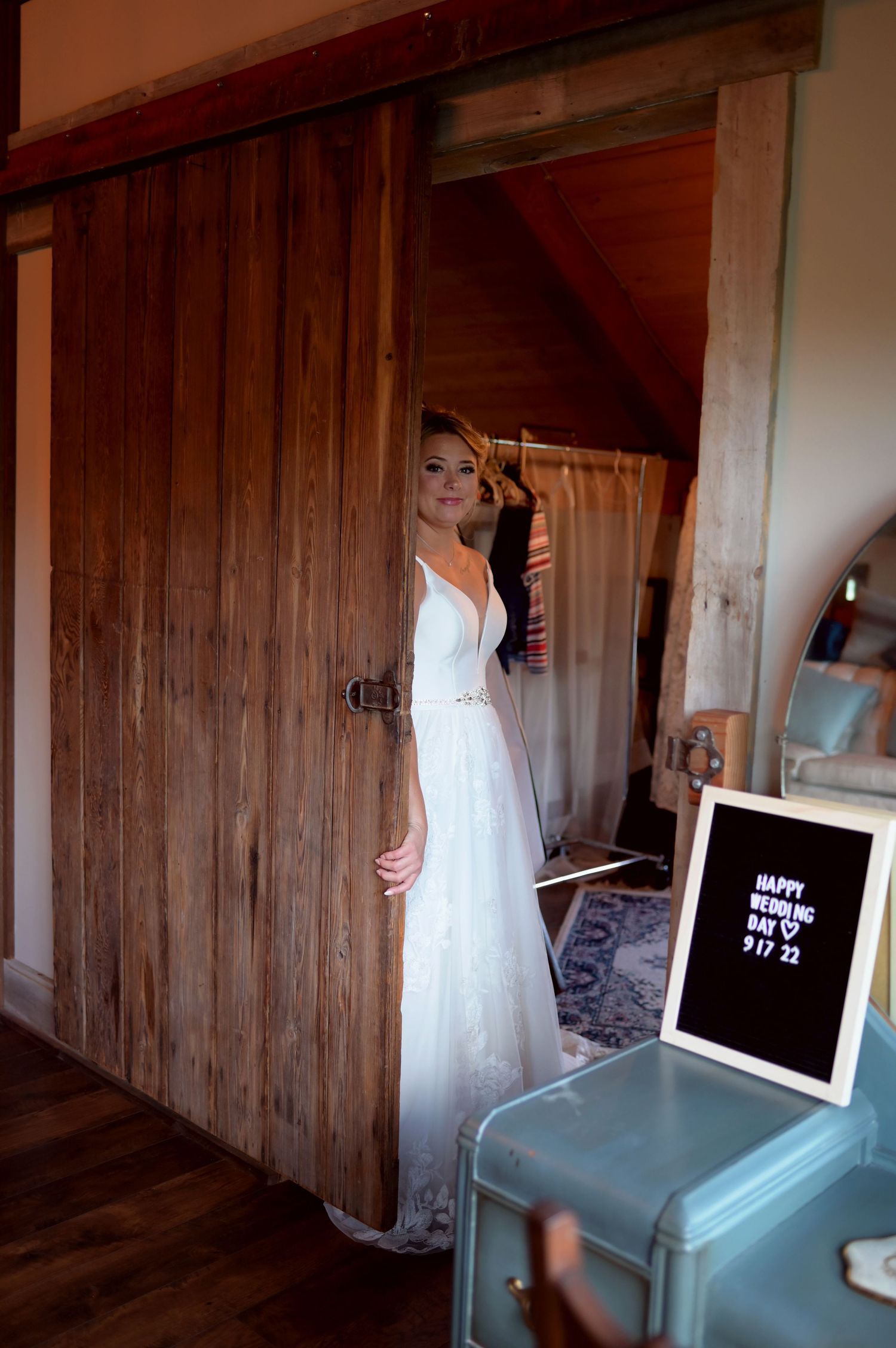 A bride in white gown standing in doorway of rustic wooden barn interior.