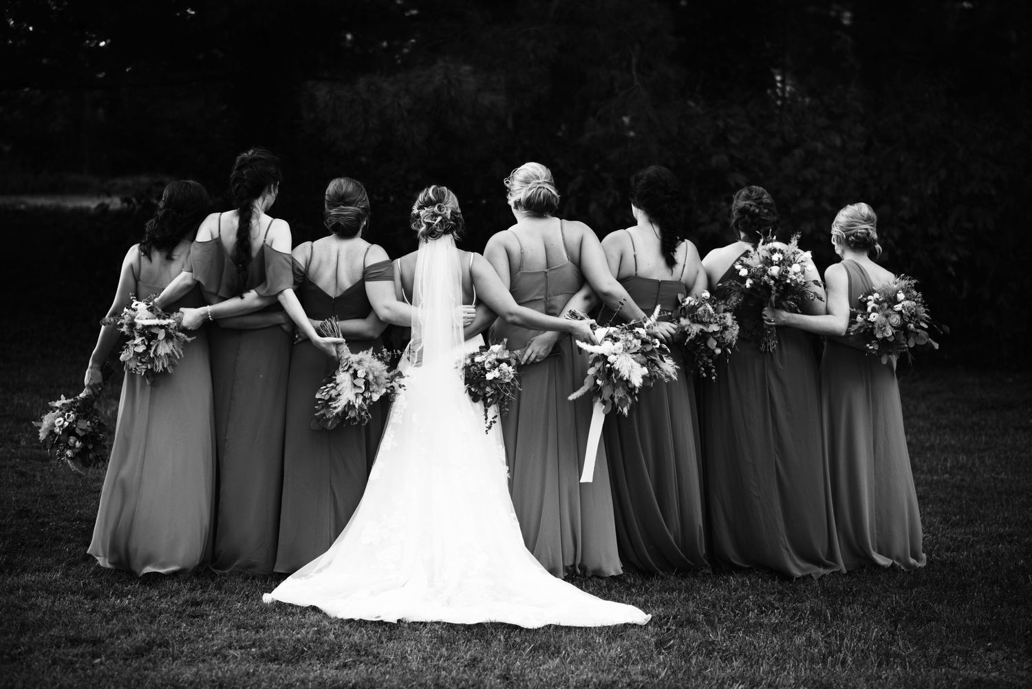 Black and white photo of bridesmaids and bride showing their bouquets from behind.