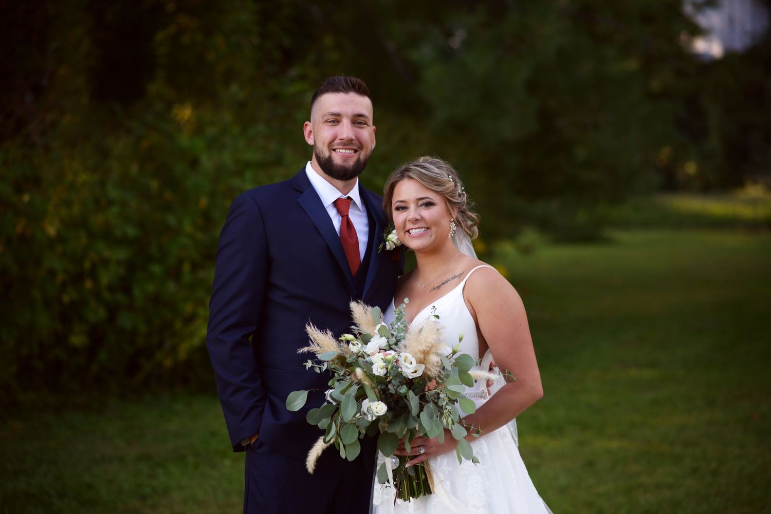 Bride and groom pose together in a garden setting with elegant floral bouquet.