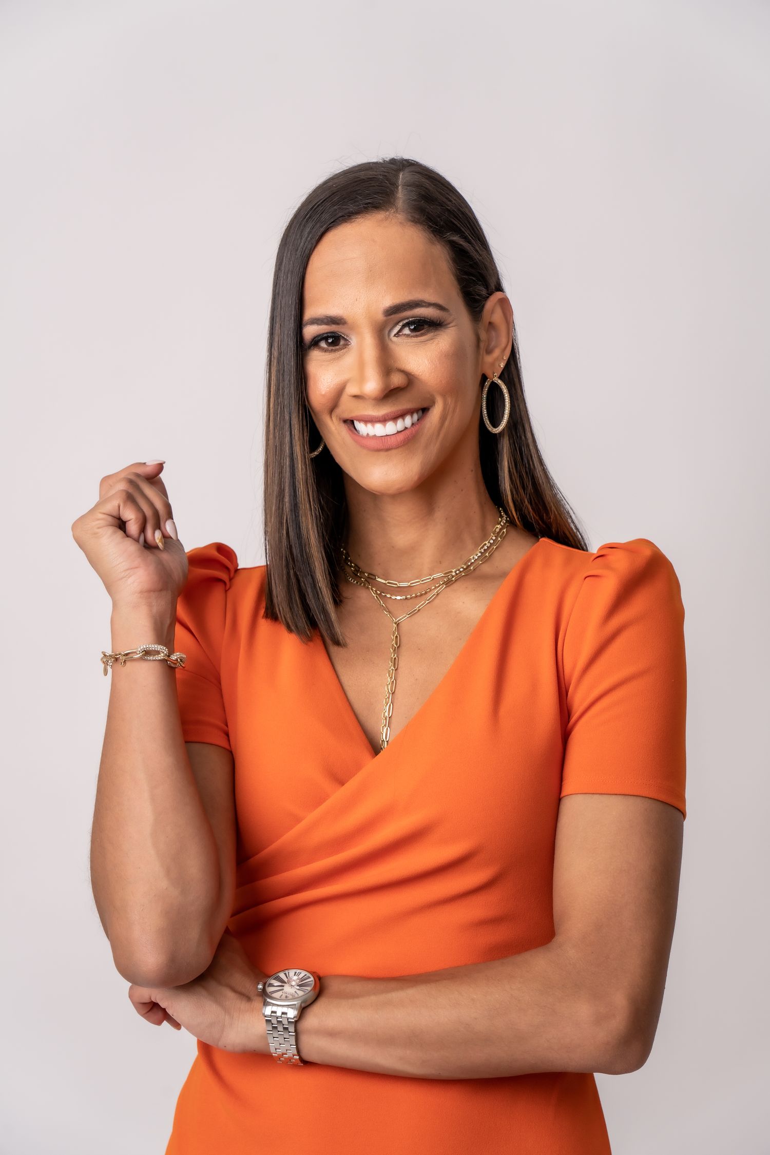 Professional portrait of woman in orange dress with jewelry against light background.