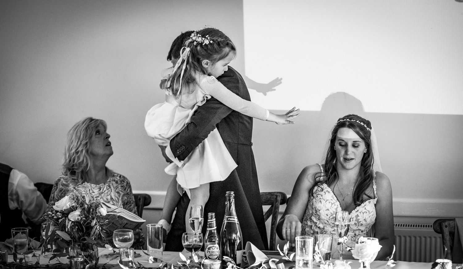 Candid black and white photo of guests enjoying lively conversation at a wedding reception table.