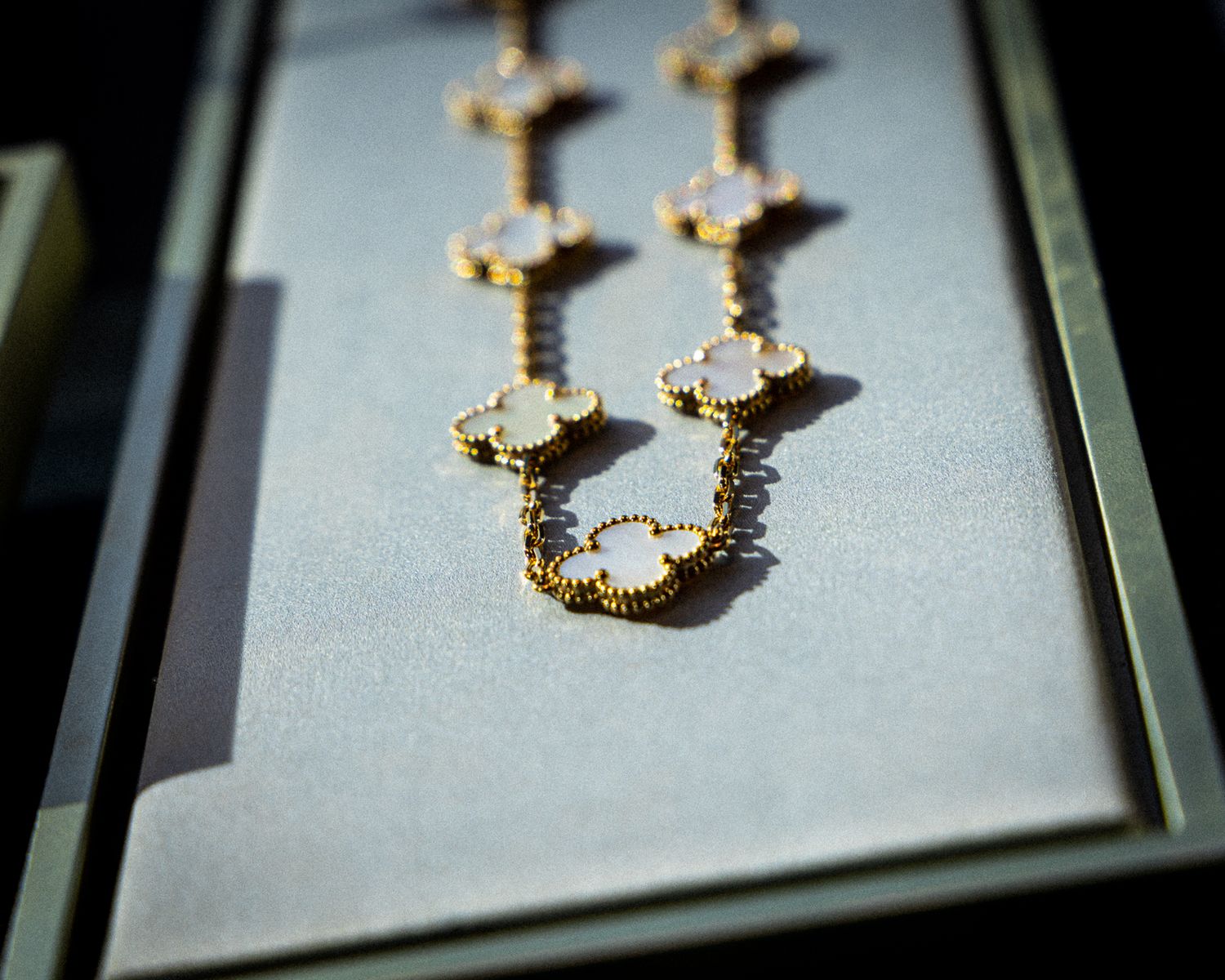 Gold-plated chain necklace with intricate cross design casts dramatic shadows on a light gray surface.