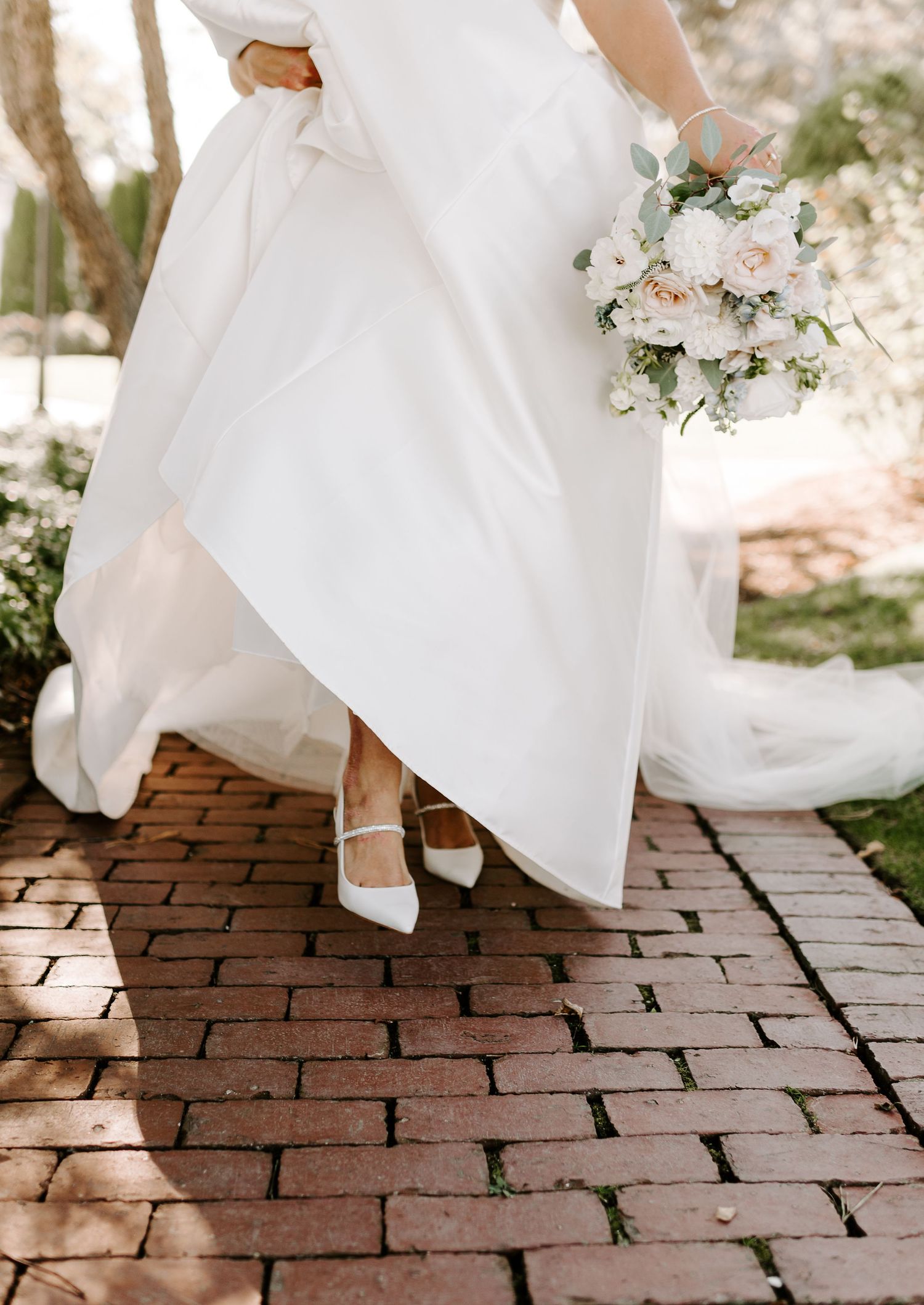 White wedding dress flows gracefully over red brick pathway during bridal portraits.