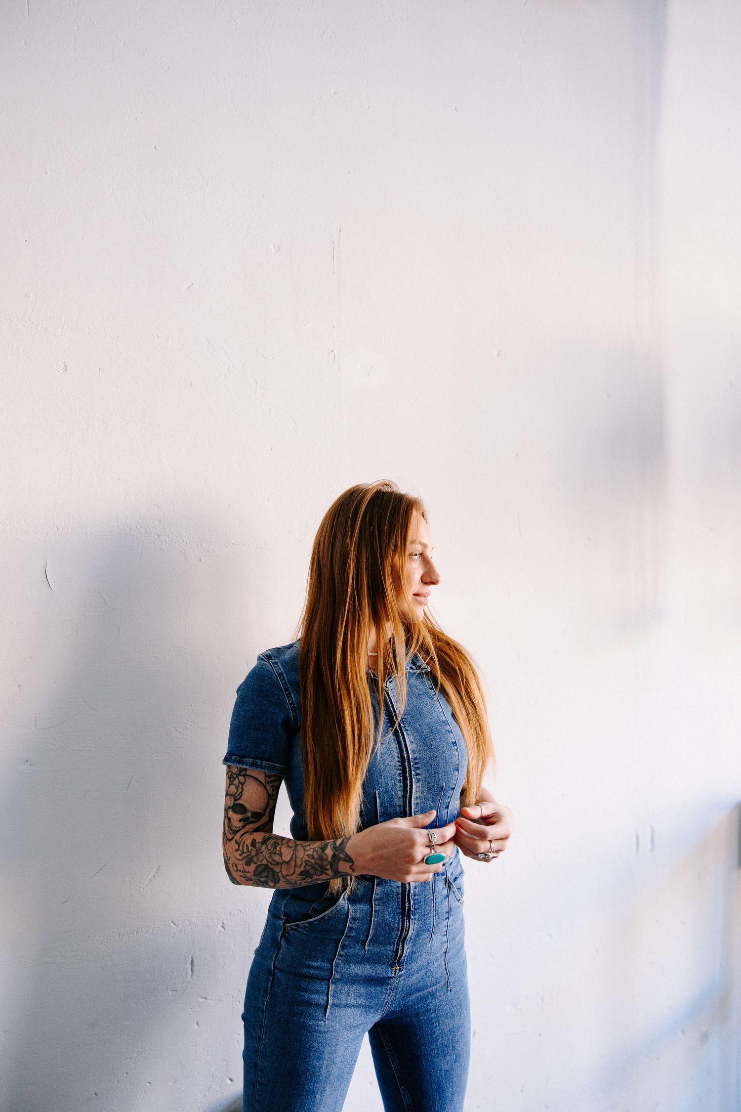 Woman in denim jumpsuit with tattoos against white background.