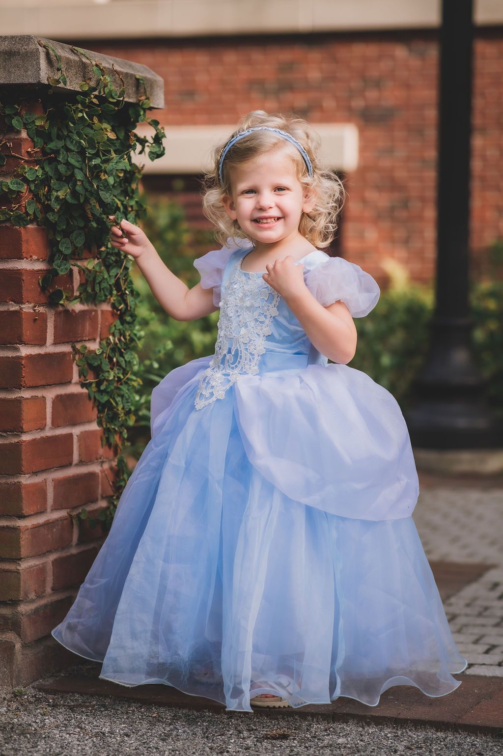 3-year-old girl stands by ivy covered brick in a Cinderella-style princess dress