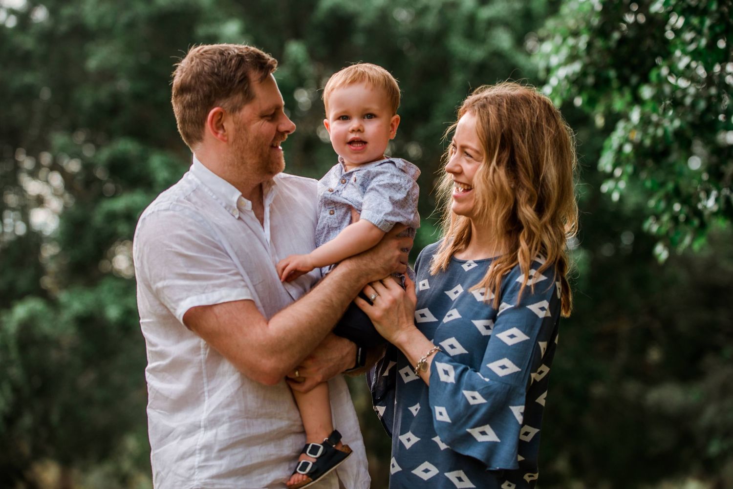 Happy family playing together outdoors in front of lush green foliage.