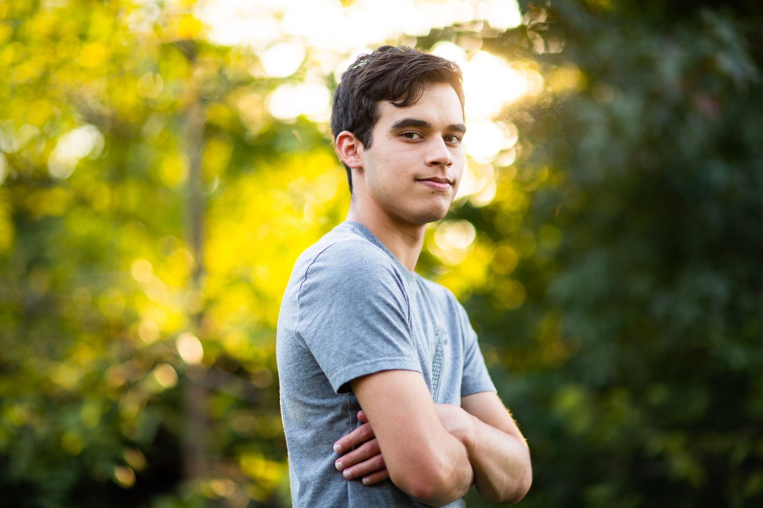 Portrait of person in grey t-shirt with arms crossed against yellow autumn background.