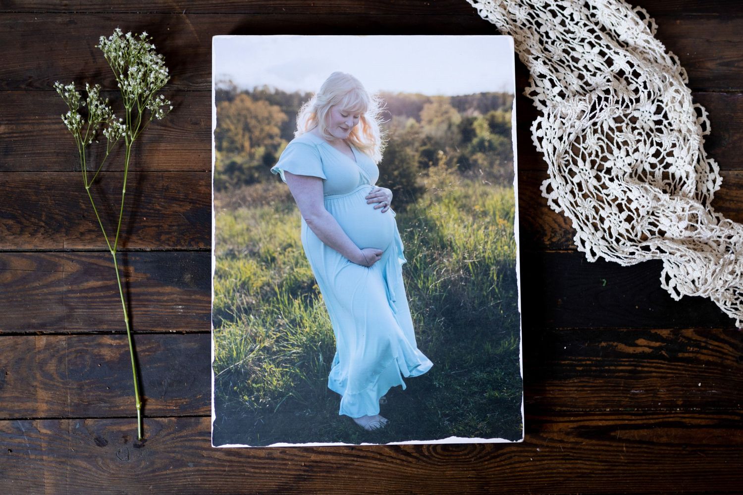 An ethereal maternity photo shows a flowing light blue dress against a golden sunset field.