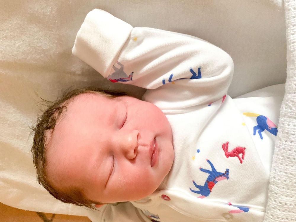 Peaceful sleeping newborn wearing a white patterned onesie.