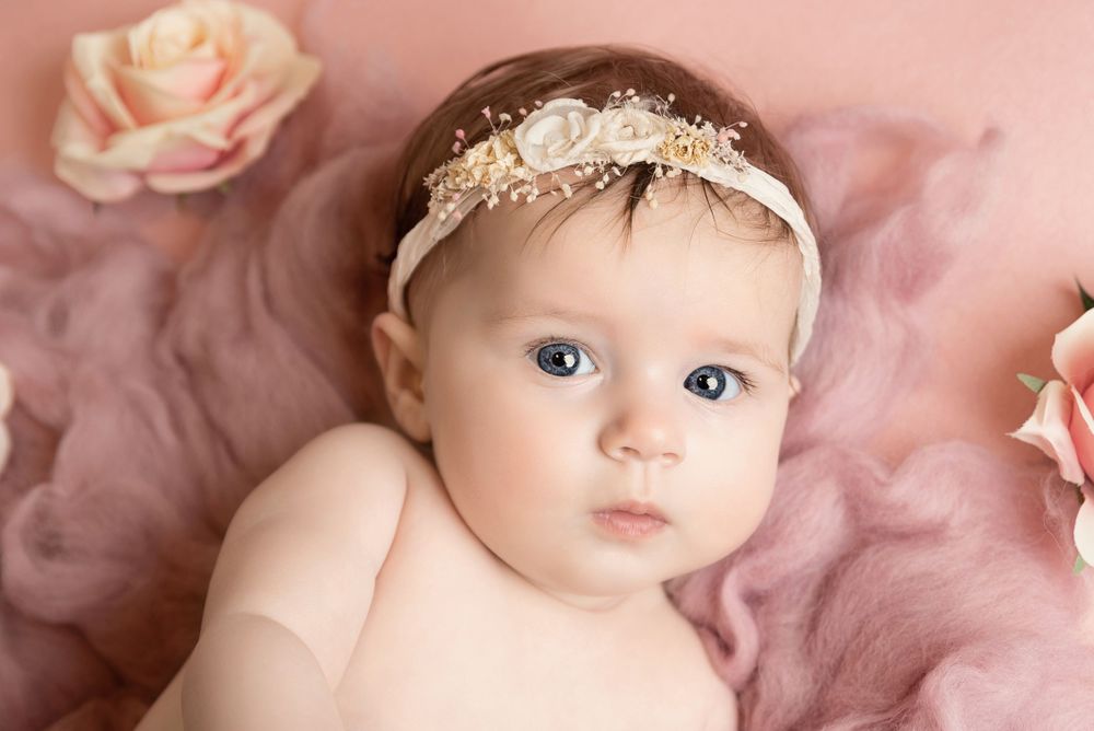 Baby portrait with delicate lace headband against pink floral backdrop.