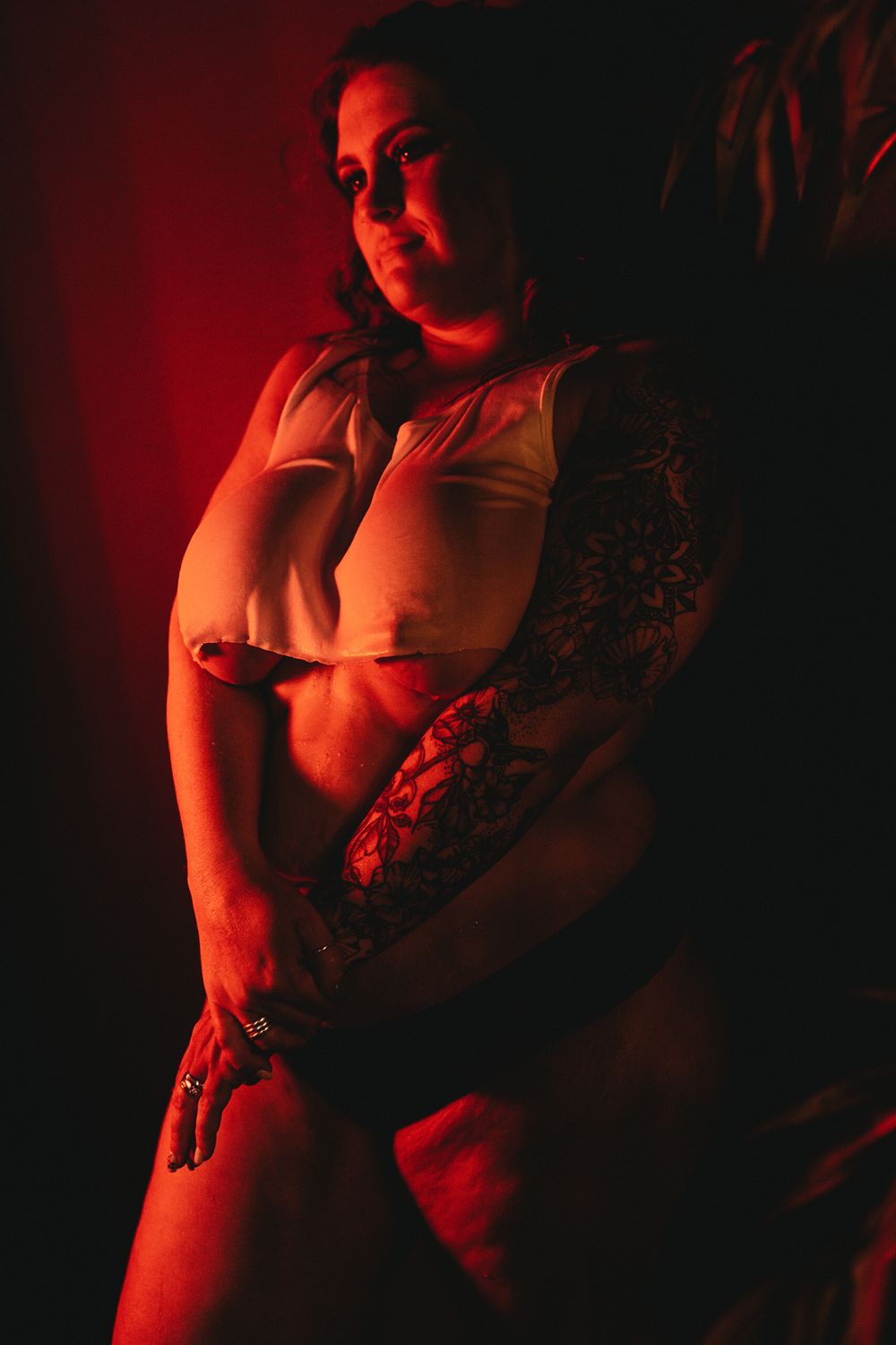 Artistic portrait with dramatic red lighting highlighting tattoo sleeve and white top.