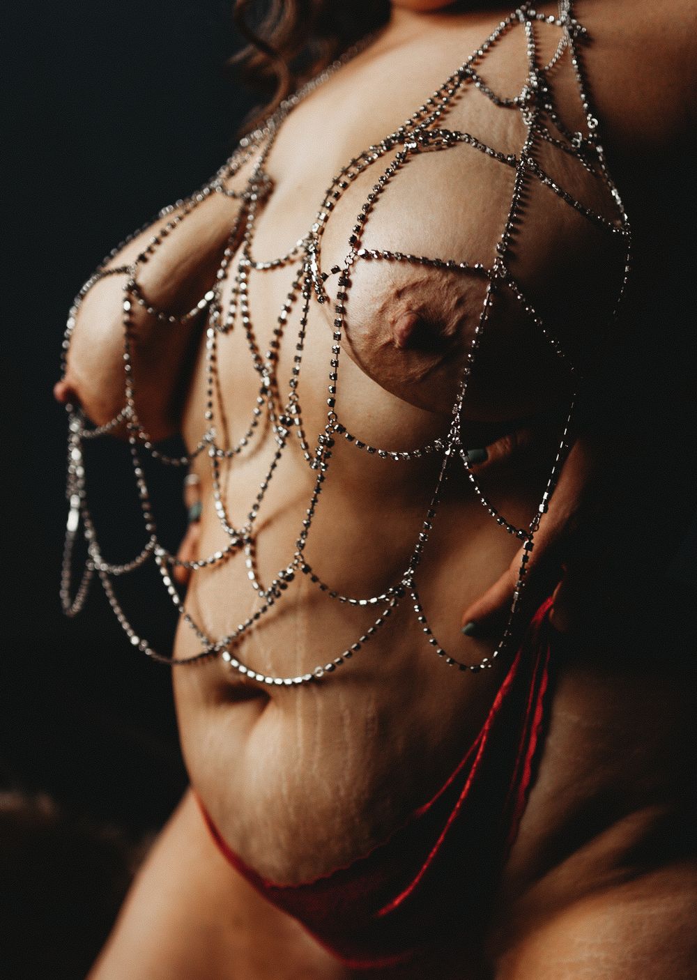 Artistic boudoir photo showing torso decorated with draped silver beaded chain jewelry against dark background.