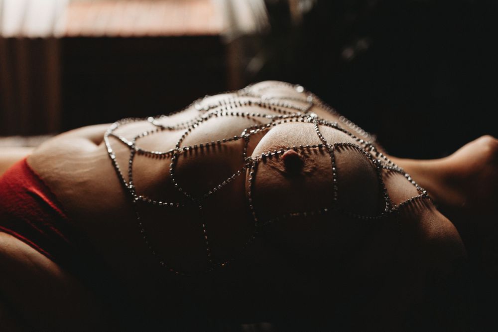 Intimate portrait with decorative body jewelry casting shadows in moody lighting.