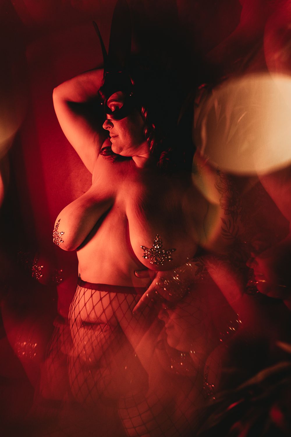 Artistic boudoir photo with red lighting and fishnet stockings featuring dramatic shadows and glitter effects.