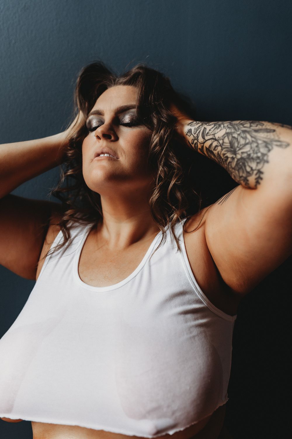 Body positive portrait against gray wall featuring white crop top and tattoo.