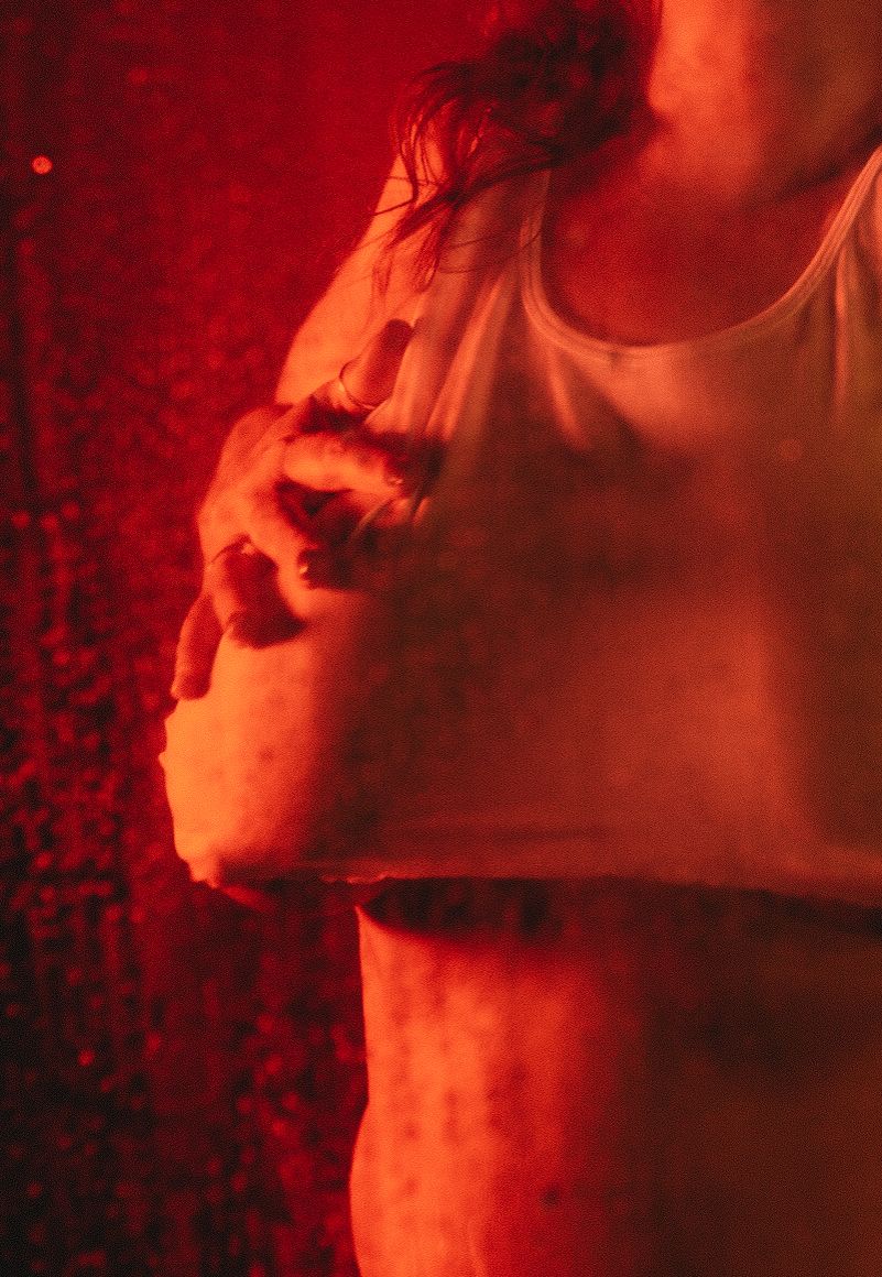 Intimate portrait bathed in red light capturing dramatic pose and emotion.