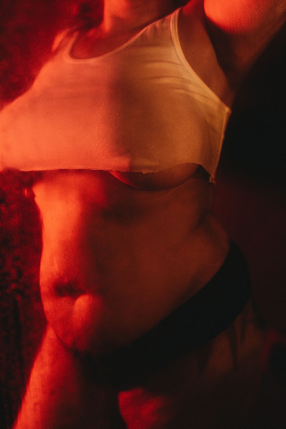 Cropped artistic photo showing torso in white tank top with dramatic red lighting.