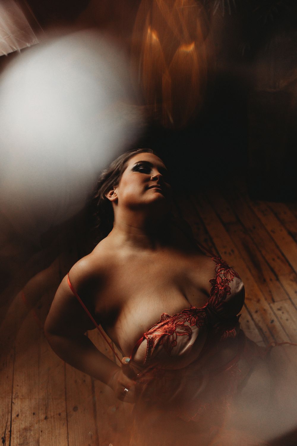 Artistic boudoir photo with moody lighting and wooden floor features red lingerie and dreamy vignette effects.