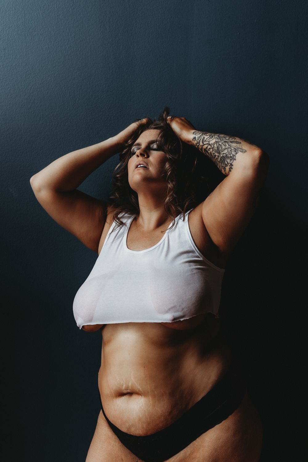Natural light bodyscape photo with white crop top against dark background.