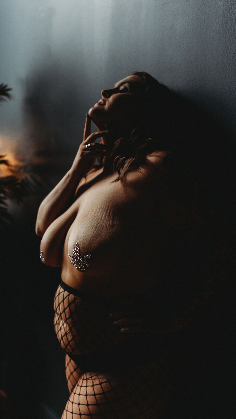 Artistic boudoir photography featuring moody lighting and fishnet stockings in a dark, atmospheric setting.