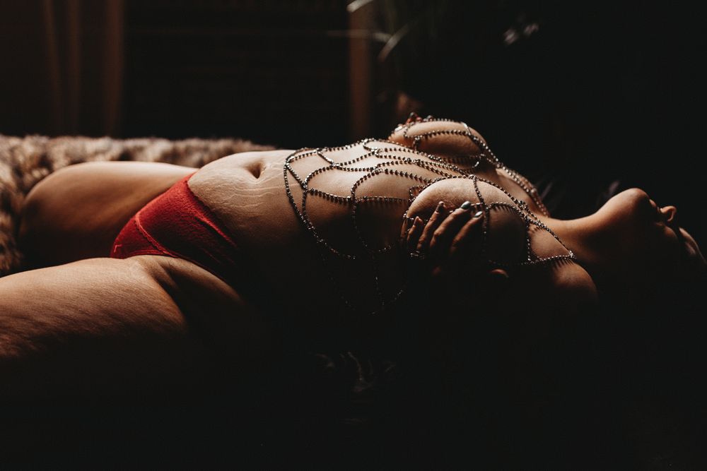 Artistic boudoir photograph with delicate body chains and dramatic lighting.