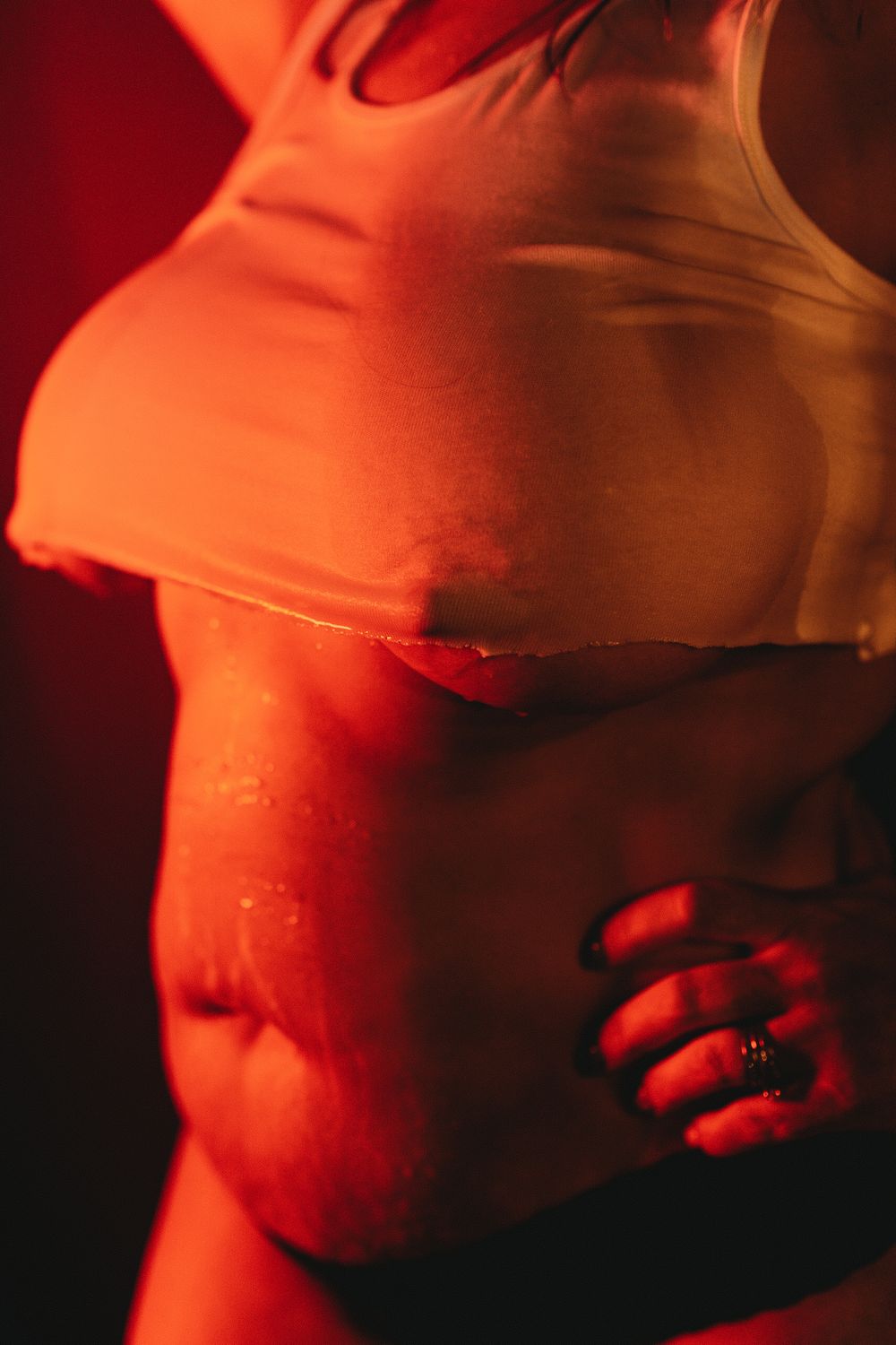 Artistic close-up photography of a torso in white top illuminated by warm red lighting with dramatic shadows.