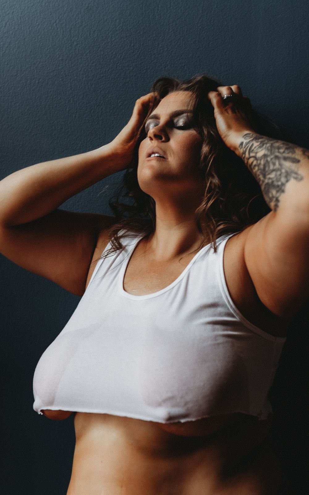 Artistic portrait against dark wall with soft lighting and white tank top.