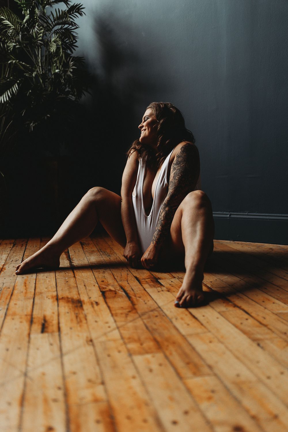 Elegant boudoir photography with natural window light and indoor palm plants.