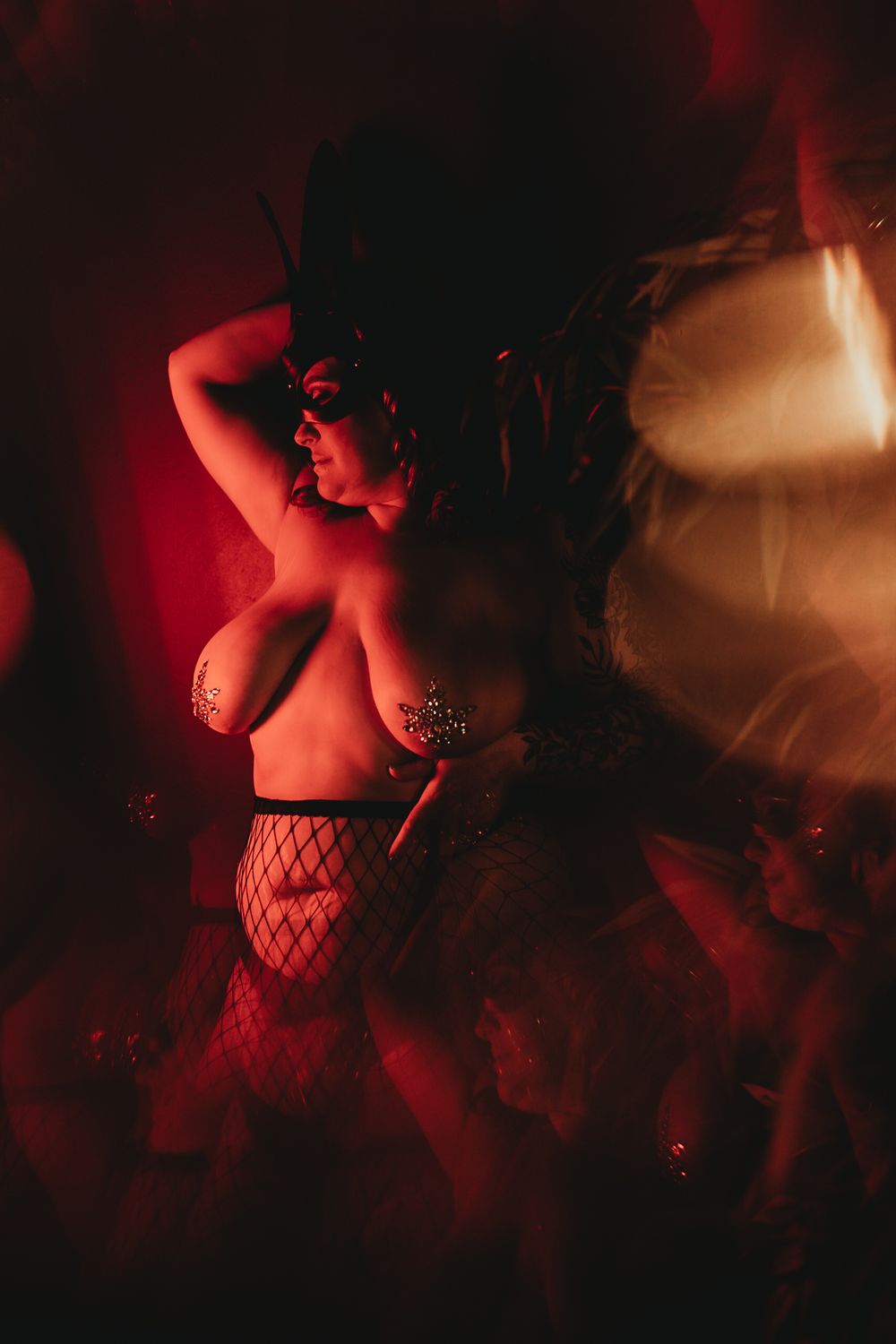 Boudoir photo in dramatic red lighting featuring fishnet stockings and artistic shadows.