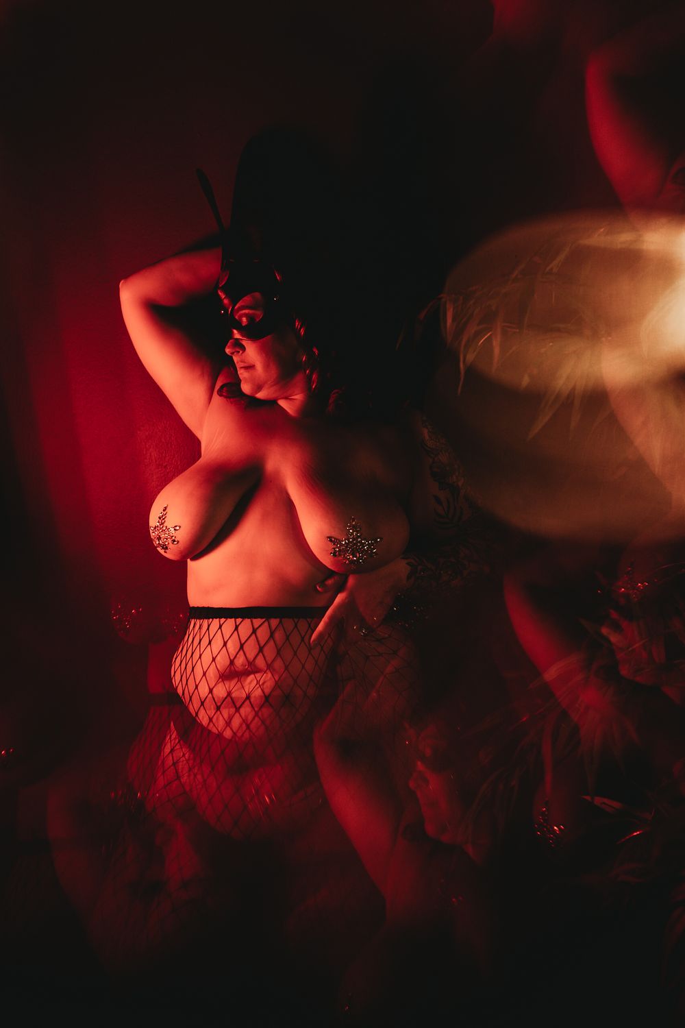 Artistic boudoir photography with red lighting and fishnets creates a moody, sensual atmosphere.