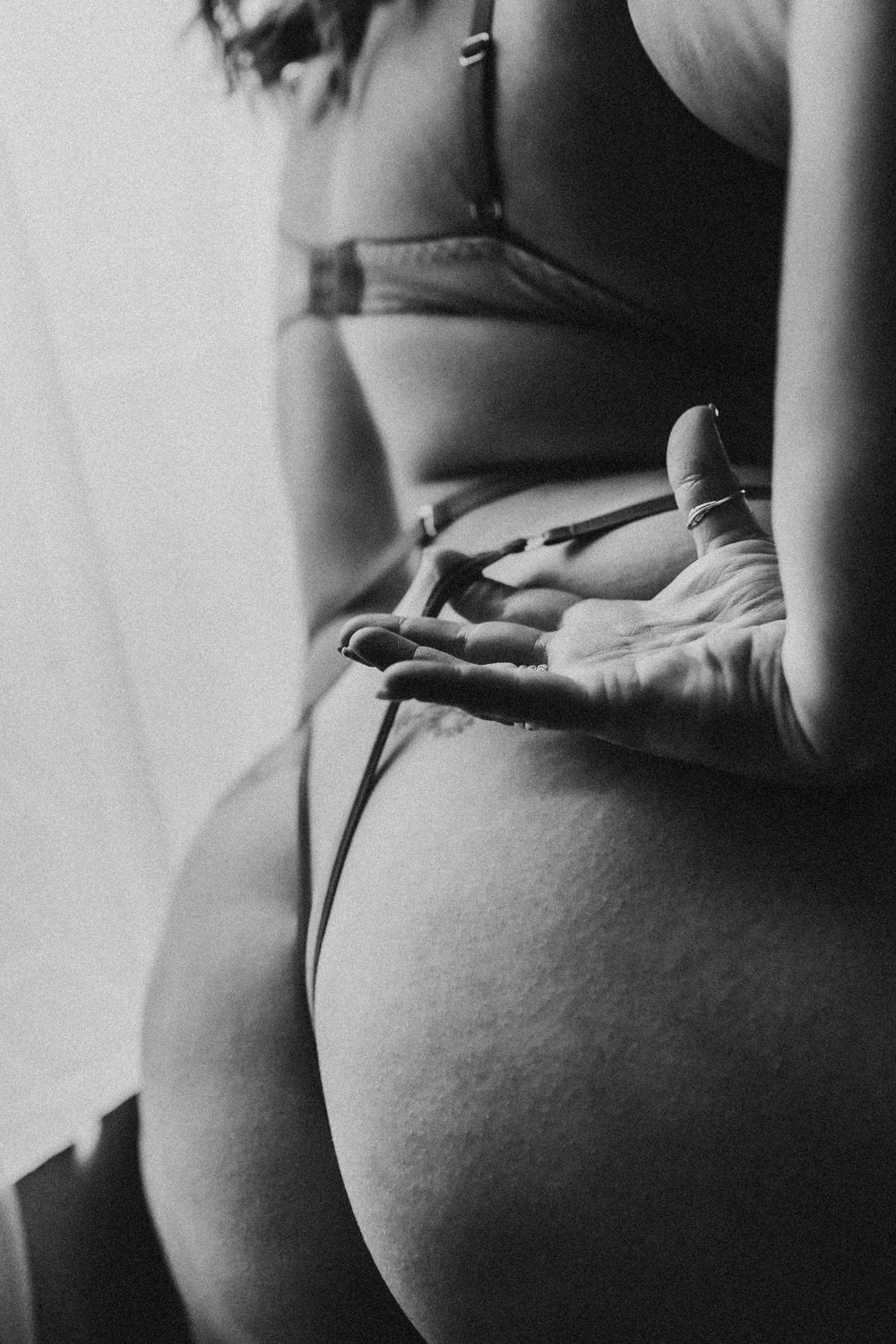 Black and white artistic intimate boudoir photo showing curves and lingerie in soft lighting.